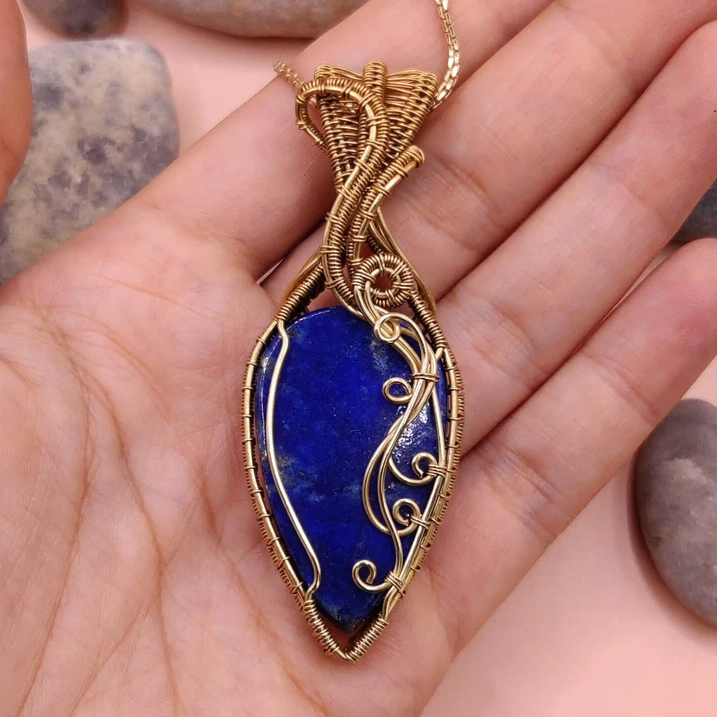 Gold-framed brass and blue lapis lazuli pendant held in a hand and made by sanguine aura handcrafted jewellery, India