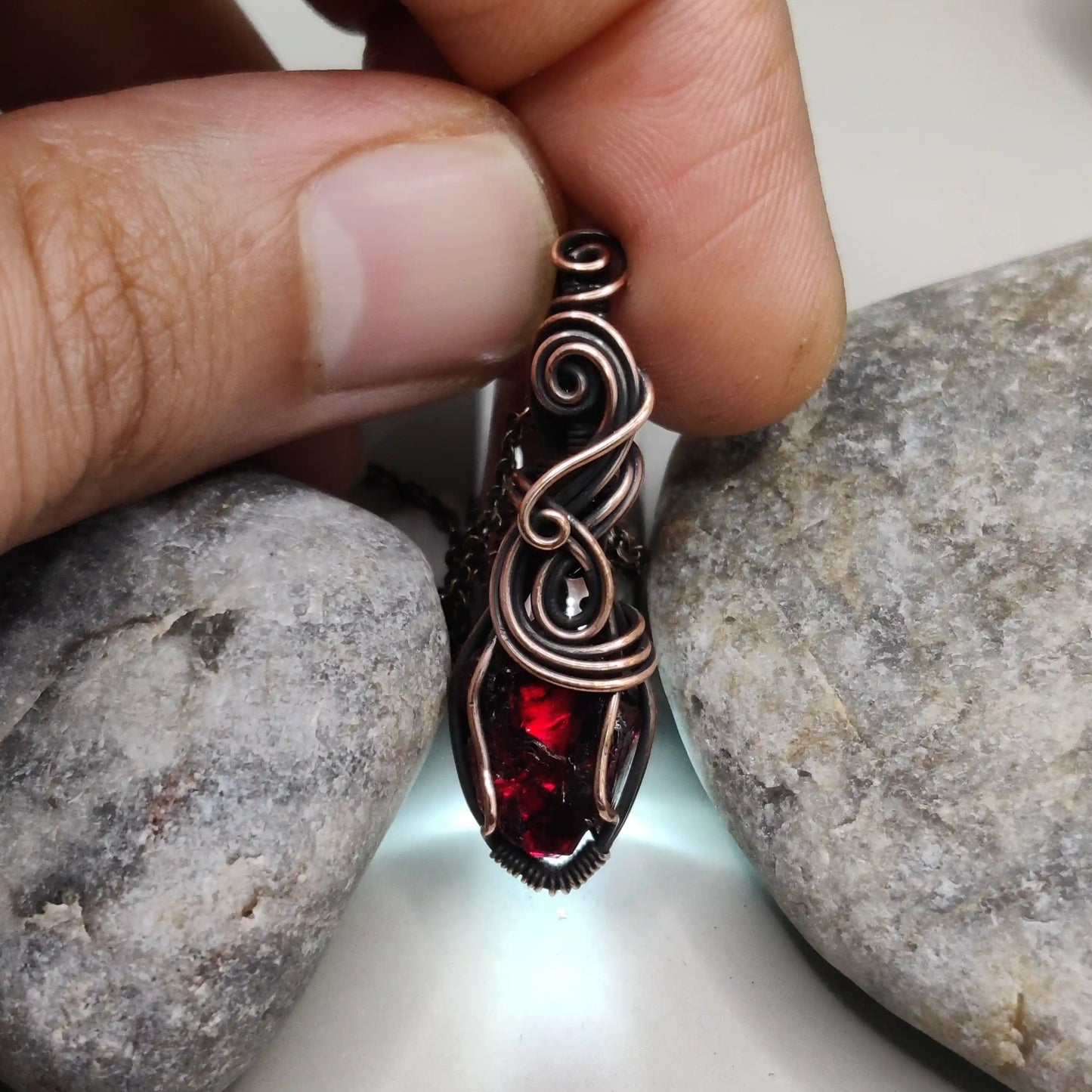 Niyati raw garnet pendant in antiqued copper 002 with light source in the background made by sanguine aura jewllery