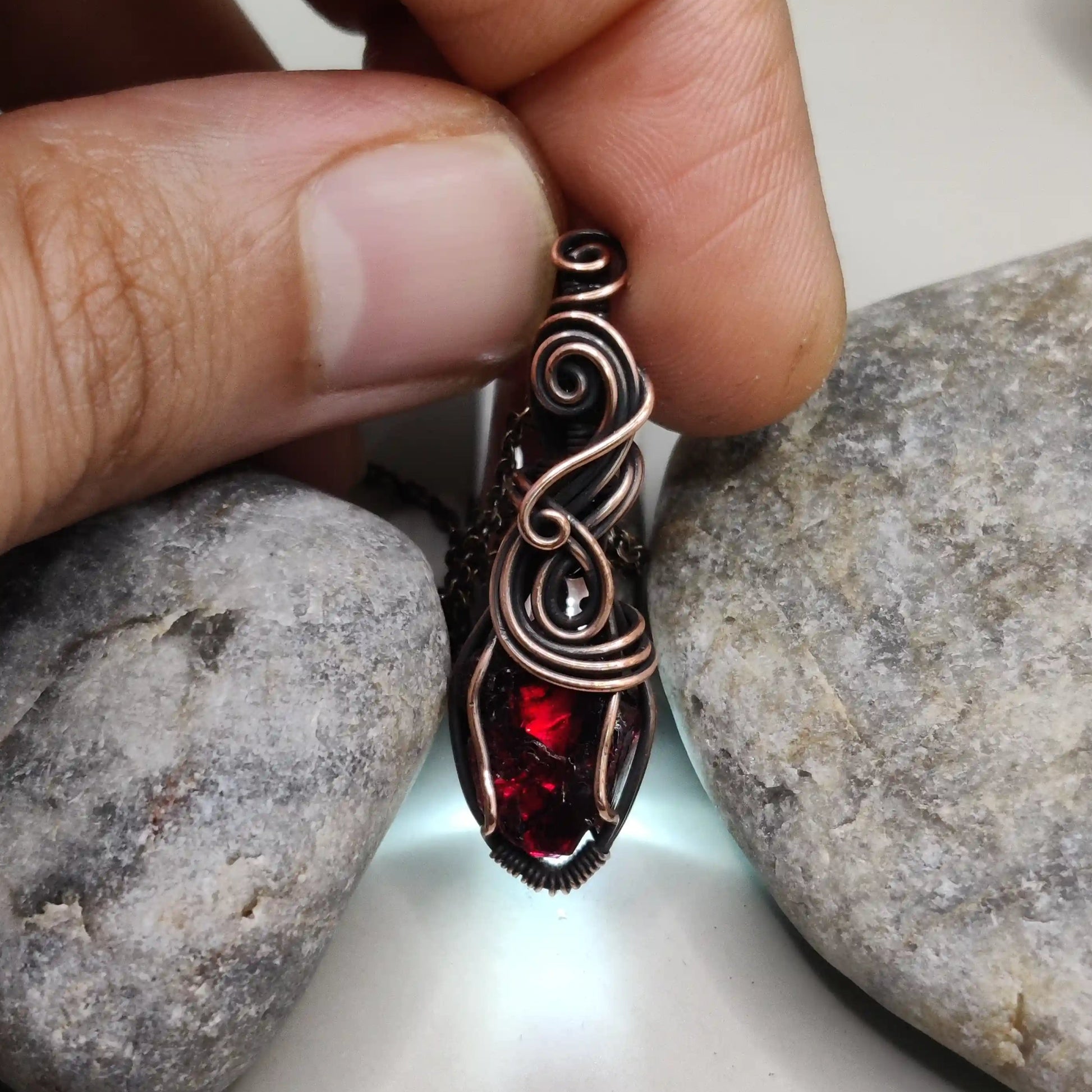 Niyati raw garnet pendant in antiqued copper 002 with light source in the background made by sanguine aura jewllery