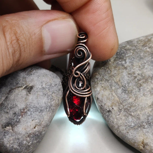 Niyati raw garnet pendant in antiqued copper 002 with light source in the background made by sanguine aura jewllery